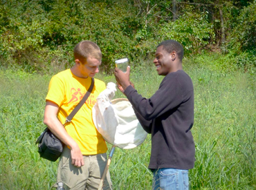 Two students out in the field look at a sample gathered in a jar.